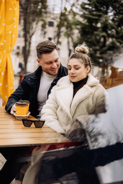 Gelukkige jonge verliefde paar in bovenkleding zittend aan een tafel buiten en koffie drinken Ontspannen in de open lucht