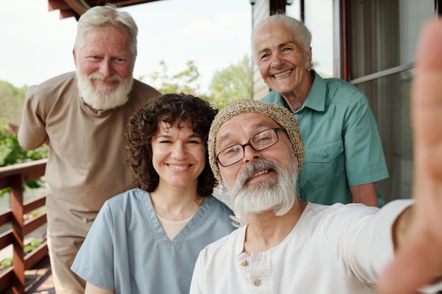 Gelukkige jonge verzorger en een groep ouderen die een selfie maken