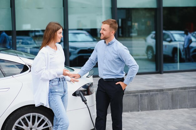 Gelukkige jonge volwassen man en glimlachende vrouw die elektrische auto oplaadt