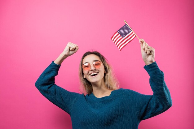 Gelukkige jonge vrouw die Amerikaanse vlag houdt tegen een studio roze achtergrond