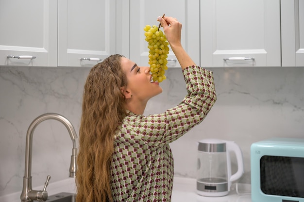 Gelukkige jonge vrouw die druiven eet in een keuken