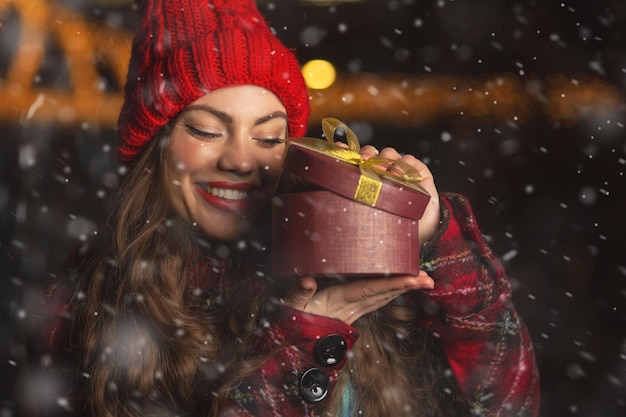 Gelukkige jonge vrouw die een geschenk ontvangt op de kerstmarkt tijdens sneeuwval. Ruimte voor tekst