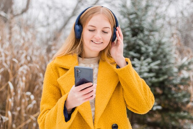 Gelukkige jonge vrouw die een jas draagt die naar muziek in hoofdtelefoons luistert