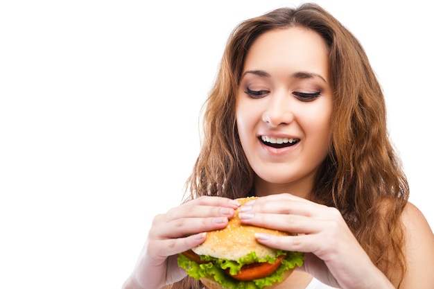 Gelukkige jonge vrouw die grote lekkere hamburger eet die op witte achtergrond wordt geïsoleerd