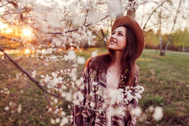 Gelukkige jonge vrouw die in de lentetuin loopt. Stijlvolle lente-outfit