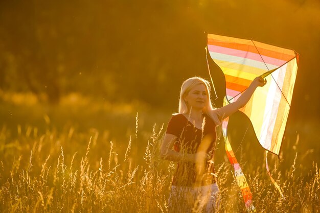 Gelukkige jonge vrouw die met een vlieger op een open plek loopt bij zonsondergang in de zomer