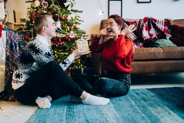 Gelukkige jonge vrouw die met kerst een cadeau van een man thuis ontvangt