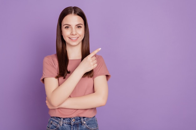 Gelukkige jonge vrouw die met vingers wijst die over violette achtergrond wordt geïsoleerd