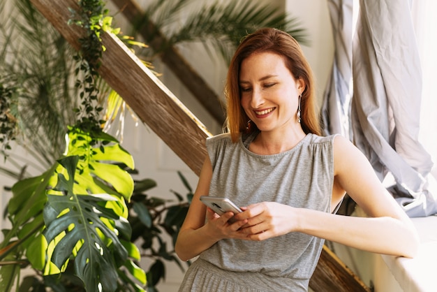 Gelukkige jonge vrouw die mobiele telefoon thuis met behulp van