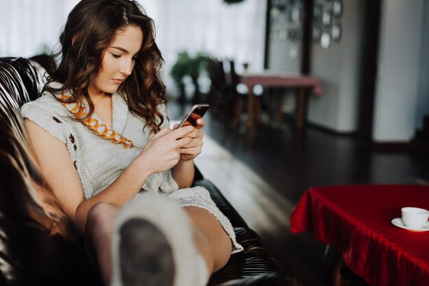 Gelukkige jonge vrouw die naar mobiele telefoon in bed kijkt