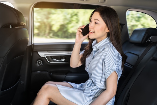 Gelukkige jonge vrouw die op de mobiele telefoon praat terwijl ze op de achterbank van de auto zit