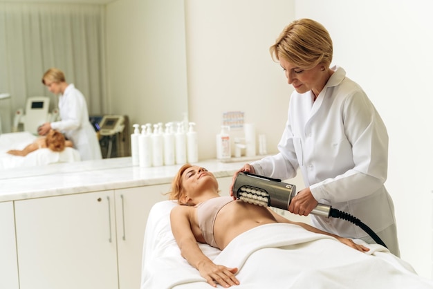 Gelukkige jonge vrouw die op een massagetafel ligt en glimlacht ze krijgt een huidbehandeling in de spa salon schoonheidsspecialiste raakt haar maag aan met speciaal gereedschap