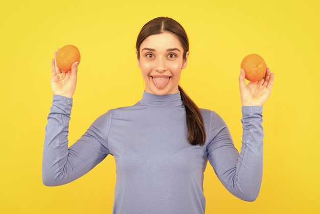 Gelukkige jonge vrouw die oranje citrusvruchten op gele organische achtergrond houdt