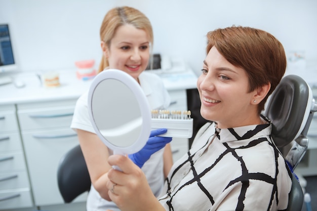 Gelukkige jonge vrouw die tanden in de spiegel controleert na het bleken van tanden