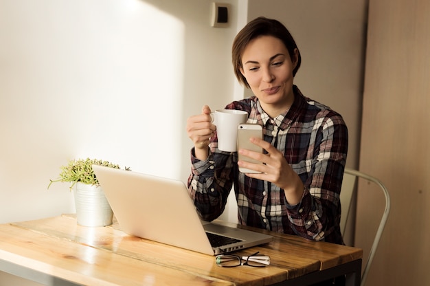 Gelukkige jonge vrouw die thuis een leuk sms of tekstbericht op haar mobiele telefoon met een glimlach bestuderen bestuderen