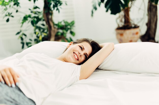Gelukkige jonge vrouw die thuis in bed ligt.