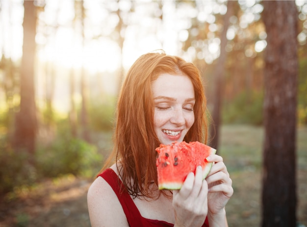 Gelukkige jonge vrouw die watermeloen op de aard eet.