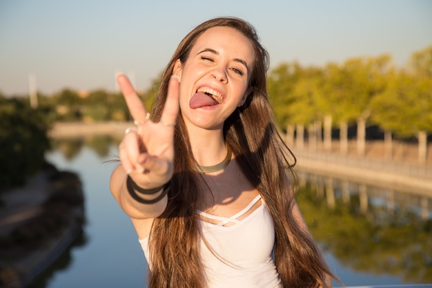 Gelukkige jonge vrouw die zich in park op zonnige dag en gesturing overwinning bevinden.