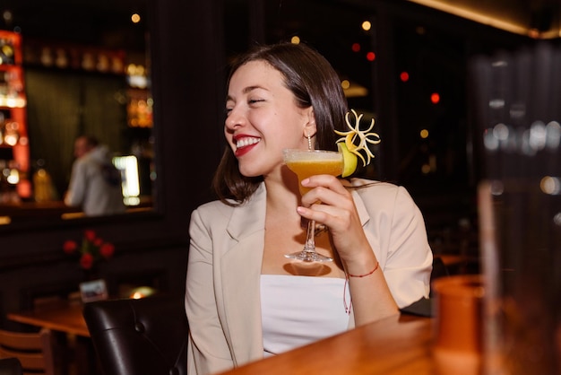 Gelukkige jonge vrouw drinkt een cocktail zittend aan een toog