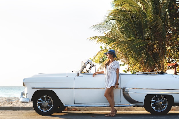 Gelukkige jonge vrouw en retro converteerbare auto naast het strand van de stad van varadero