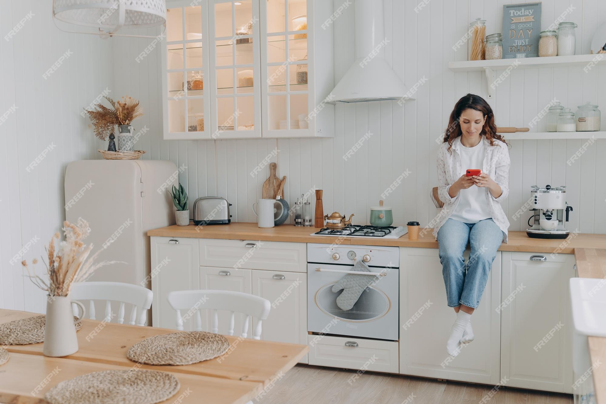 Begin Doorlaatbaarheid Gietvorm Gelukkige jonge vrouw heeft bericht op telefoon meisje zit op het aanrecht  in de keuken in haar appartement | Premium Foto