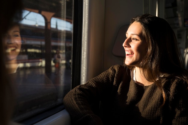 Gelukkige jonge vrouw in een trein die uit het raam kijkt