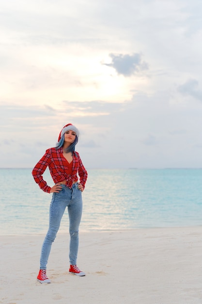 Gelukkige jonge vrouw in kerstmuts op het strand in de buurt van het zeereisconcept