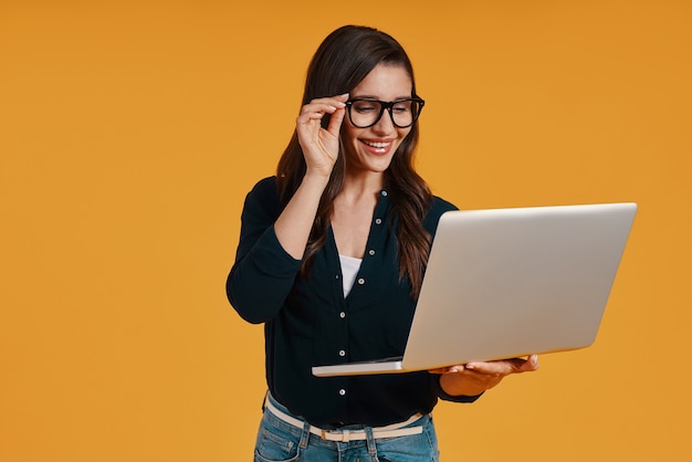 Gelukkige jonge vrouw in slimme vrijetijdskleding die laptop gebruikt en glimlacht