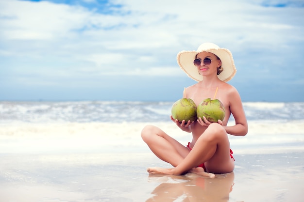 Gelukkige jonge vrouw in strohoed op het strand met een kokosnootdrankje