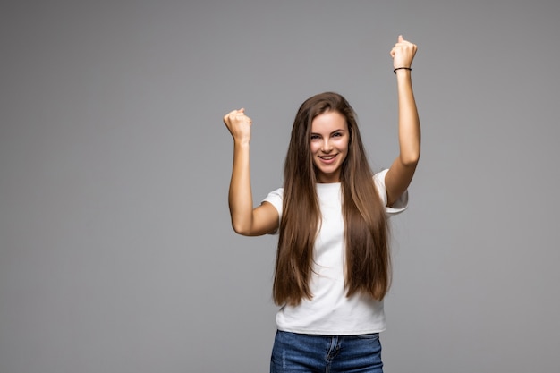 Gelukkige jonge vrouw in vrijetijdskleding gebaren en ogen gesloten houden terwijl ze tegen een grijze achtergrond staat