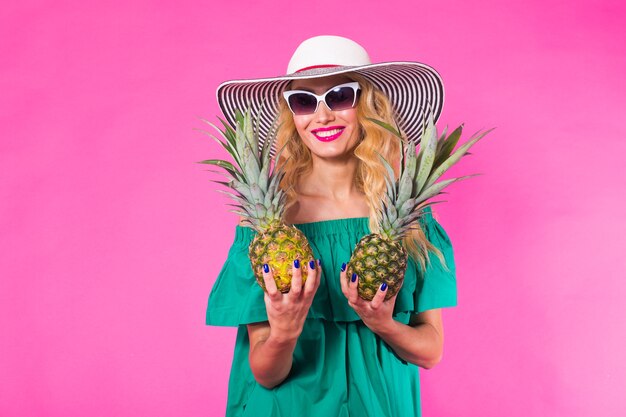 Gelukkige jonge vrouw met een ananas op een roze achtergrond. Zomer, dieet en vakantie concept