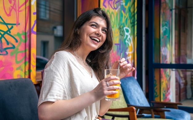 Gelukkige jonge vrouw met een glas limonade tegen een fel geschilderde muur