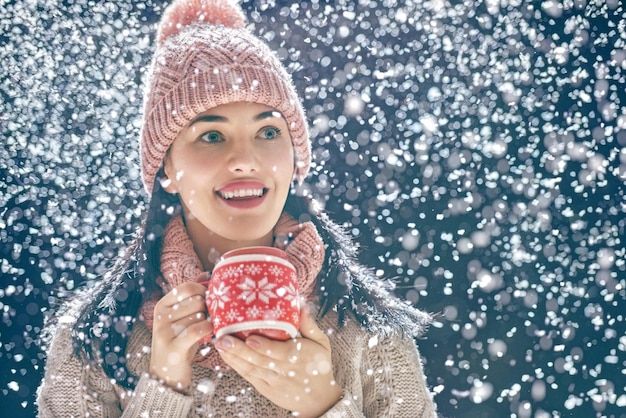 Gelukkige jonge vrouw met een kopje hete thee op besneeuwde winterwandeling in de natuur