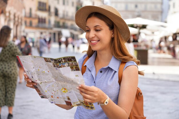 Foto gelukkige jonge vrouw met een stadsplattegrond, strohoed en rugzak op reis