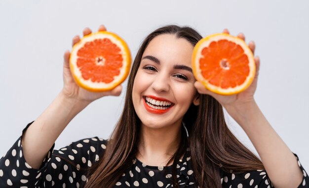 Gelukkige jonge vrouw met grapefruit helften in de buurt van gezicht. Vrolijke glimlach met rode lippen.