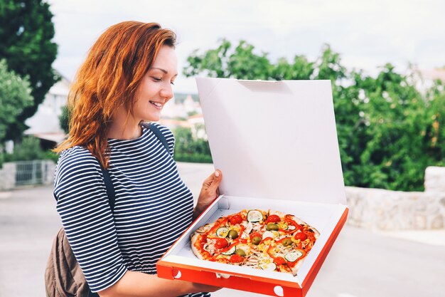 Gelukkige jonge vrouw met hete pizza in doos, buiten in europese straat