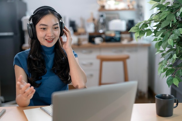 Gelukkige jonge vrouw met koptelefoon die webconferentie houdt terwijl ze thuis werkt