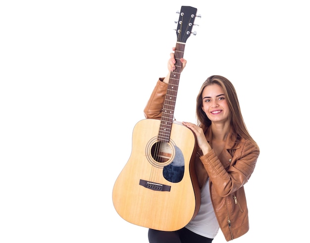 Gelukkige jonge vrouw met lang haar in bruine jas met een gitaar op een witte achtergrond in studio