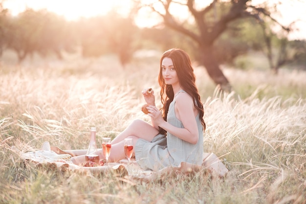 Gelukkige jonge vrouw met picknick in de weide met een glas wijn