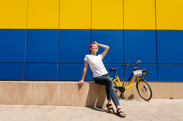 Gelukkige jonge vrouw met roze haar loopt in de zomer op de fiets door de stad.