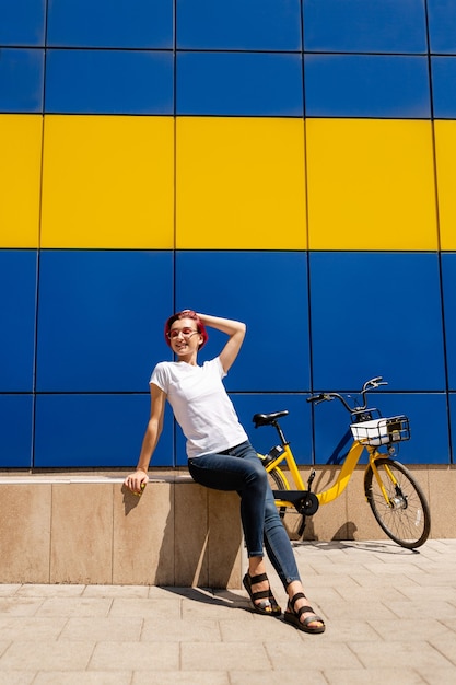 Gelukkige jonge vrouw met roze haar loopt in de zomer op de fiets door de stad.