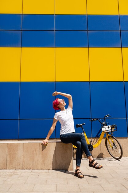 Gelukkige jonge vrouw met roze haar loopt in de zomer op de fiets door de stad.