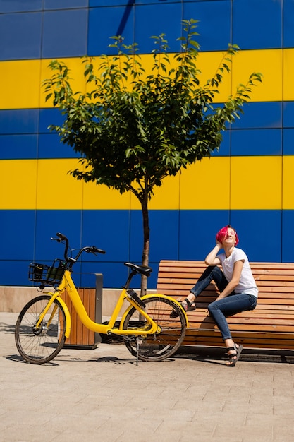 Gelukkige jonge vrouw met roze haar loopt in de zomer op de fiets door de stad.