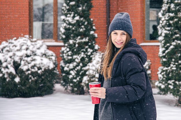 Gelukkige jonge vrouw met thermomok bij sneeuwweer