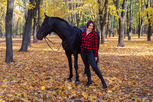 gelukkige jonge vrouw naast zwart paard in de herfst in het park