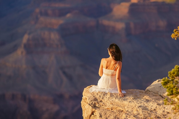 Gelukkige jonge vrouw op een steile klif die geniet van het prachtige uitzicht over de beroemde Grand Canyon bij zonsondergang Grand Canyon National Park Arizona USA