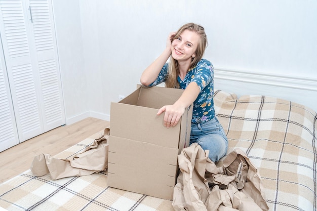 Gelukkige jonge vrouw zit op bed met een open kartonnen doos thuis en levert een pakketje uit.