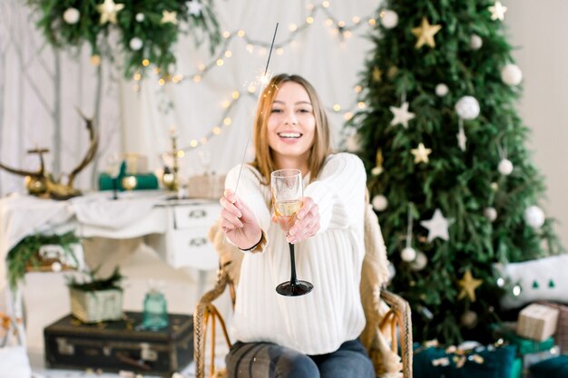 Gelukkige jonge vrouw zit voor de kerstversiering en houdt Bengalen licht