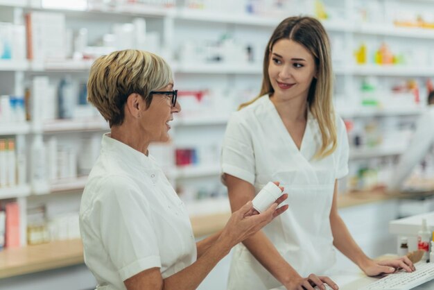 Gelukkige jonge vrouwelijke apotheker die met senior collega werkt