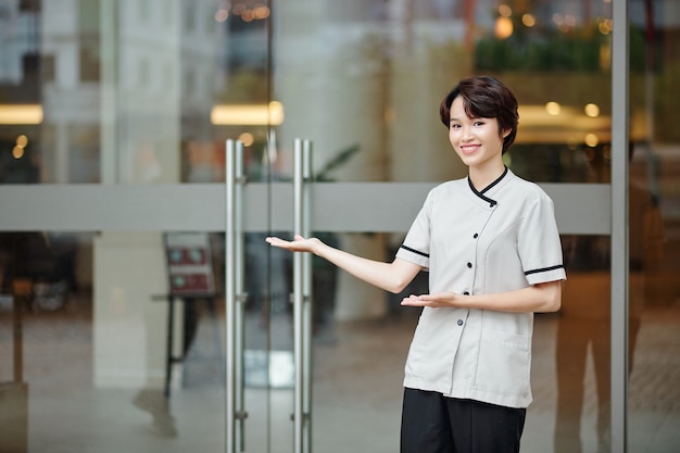 Gelukkige jonge vrouwelijke conciërge die een verwelkomend gebaar maakt en gasten in het hotel uitnodigt